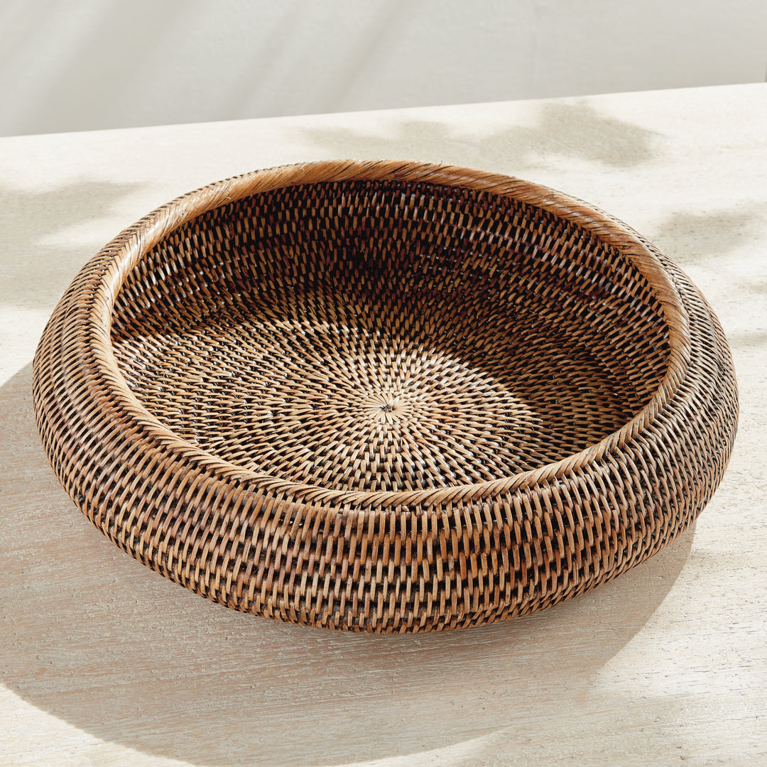 Brown rattan shallow display bowl viewed from above on a pale tabletop, showing its empty woven base - Coastal Transitional