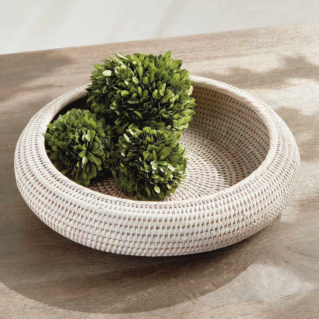 Whitewash rattan shallow display bowl holding three leafy green decorative balls on a pale tabletop - Coastal Transitional